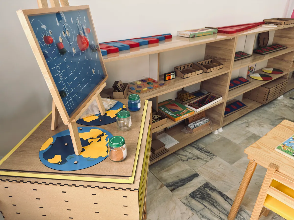 Matériel Montessori sur des étagères basses : barres rouges et bleues, puzzles des continents et tableau du système solaire.