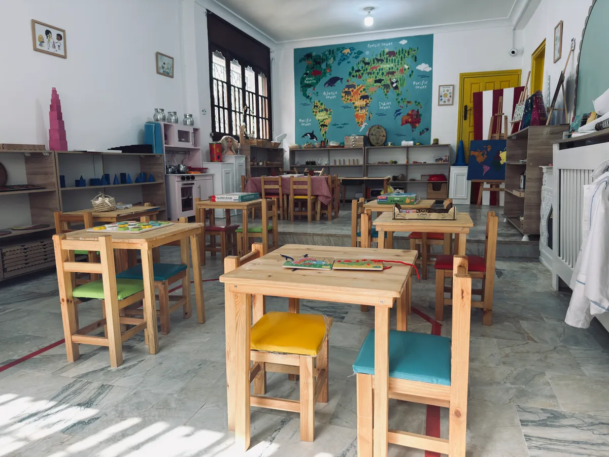 Petites tables en bois aux assises colorées, tour rose Montessori et carte du monde en arrière-plan.