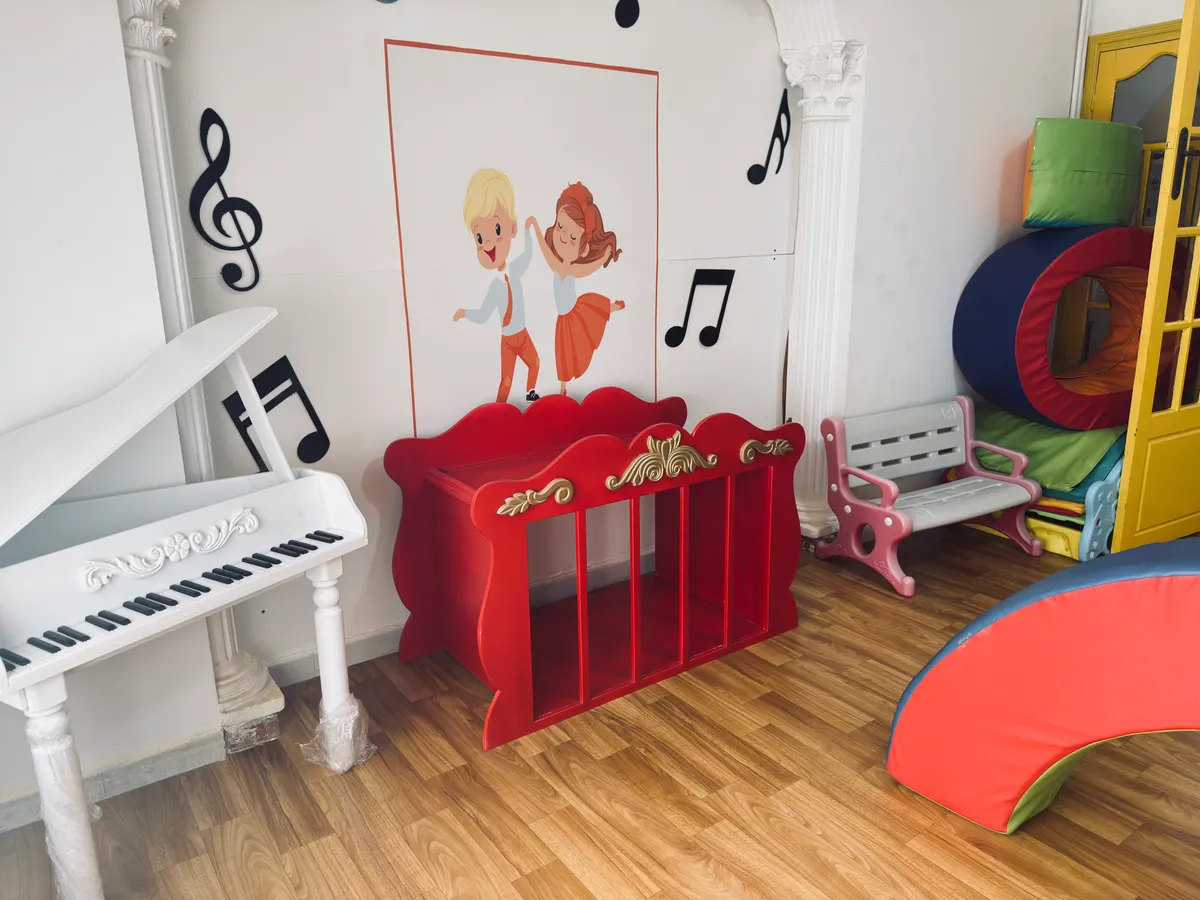 Coin musique : petit piano blanc, meuble rouge et notes de musique décorant le mur.