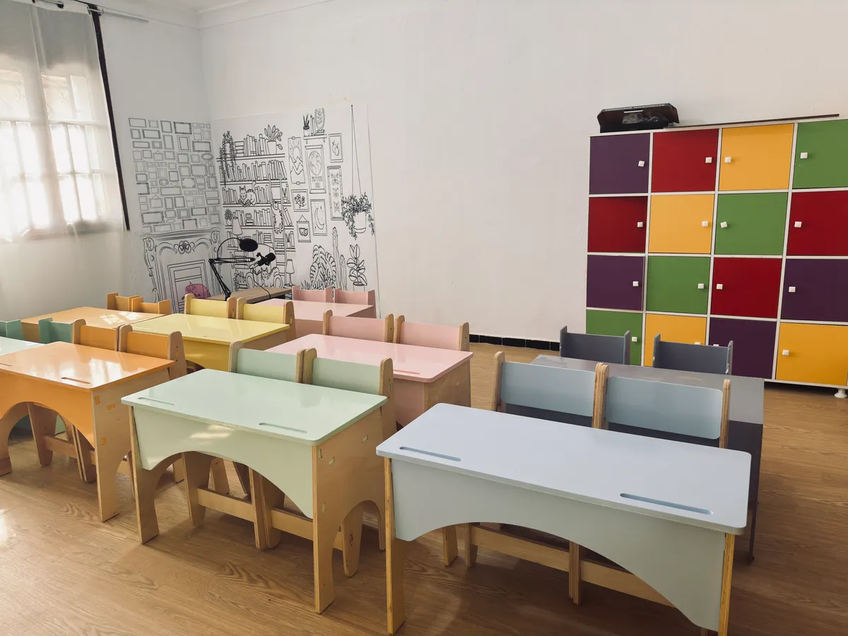 Classe aux bureaux pastel avec casiers de rangement colorés et mur illustré.