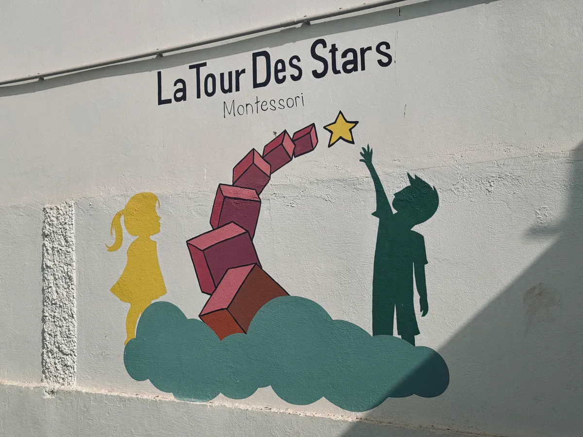 Fresque murale « La Tour des Stars Montessori » : deux silhouettes d’enfants, une tour de cubes roses et une étoile.