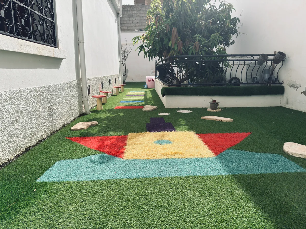 Jardin en gazon synthétique : chemin de pas japonais, formes colorées au sol et plantes.