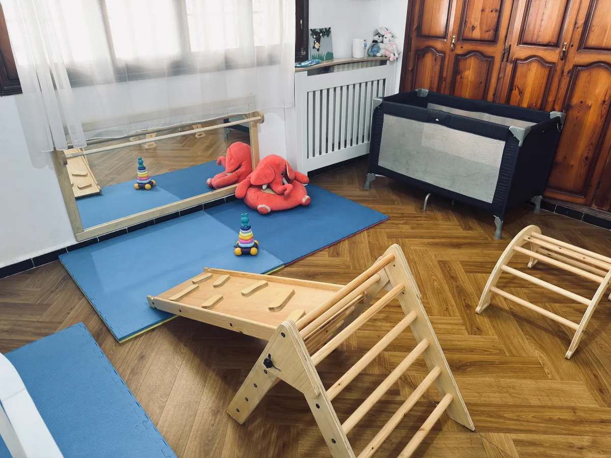 Espace des tout-petits : triangle d’escalade en bois avec rampe, miroir bas et tapis de sol.