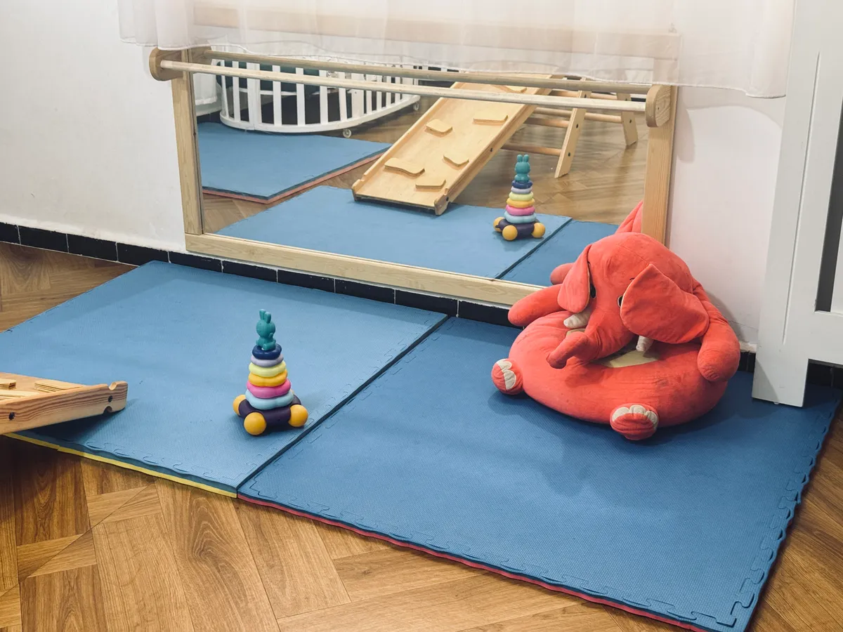 Tapis d’éveil devant un miroir bas, avec anneaux à empiler et grande peluche.