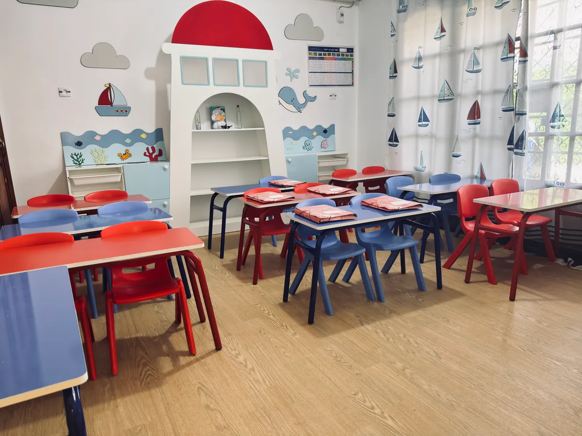 Classe sur le thème de la mer : étagère phare, tables bleues et rouges, rideaux à voiliers.